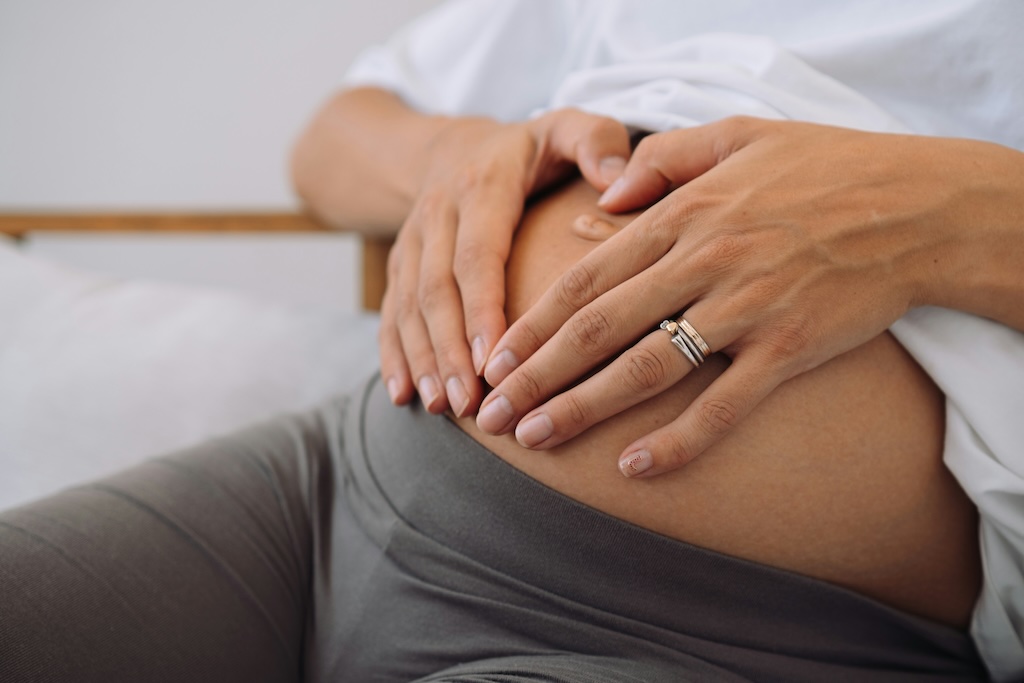 A woman making a heart shape with her hands on her pregnancy bump